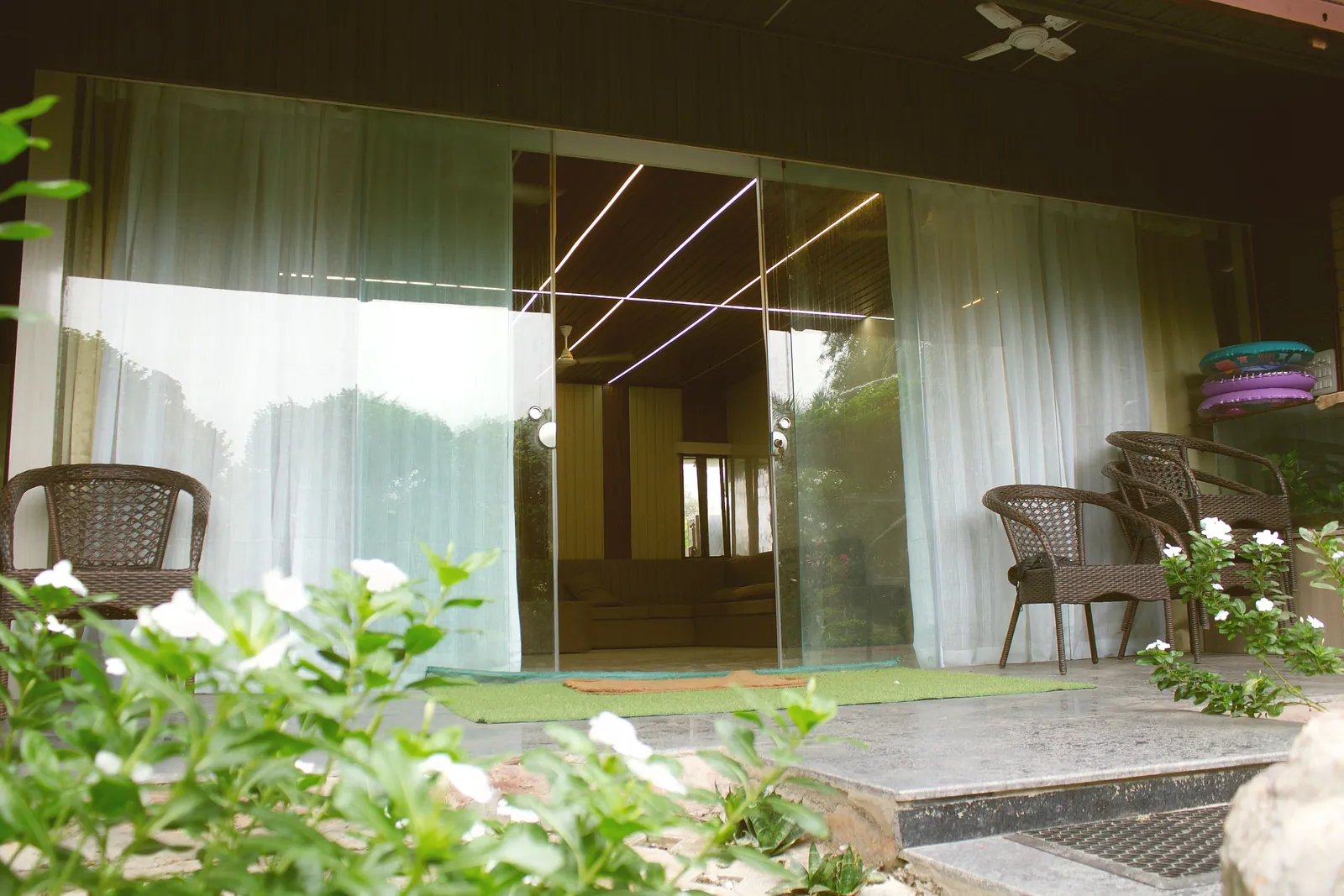 Wicker chairs on the veranda in front of the glass walls and white curtains of the farmhouse at Raj Organic Farm