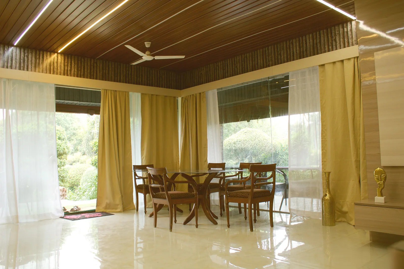 The living and dining area at Raj Organic Farm, with a wood-slat ceiling, golden curtains and glass walls to the garden
