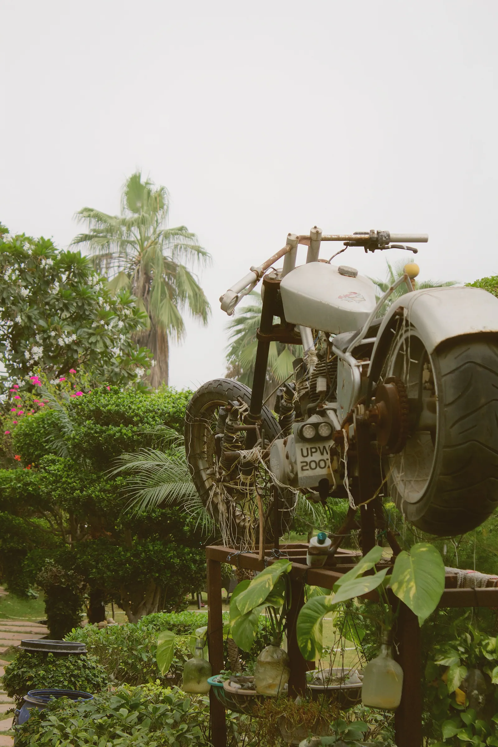 A motorbike sculpture on a metal stand among flowering plants in the garden at Raj Organic Farm