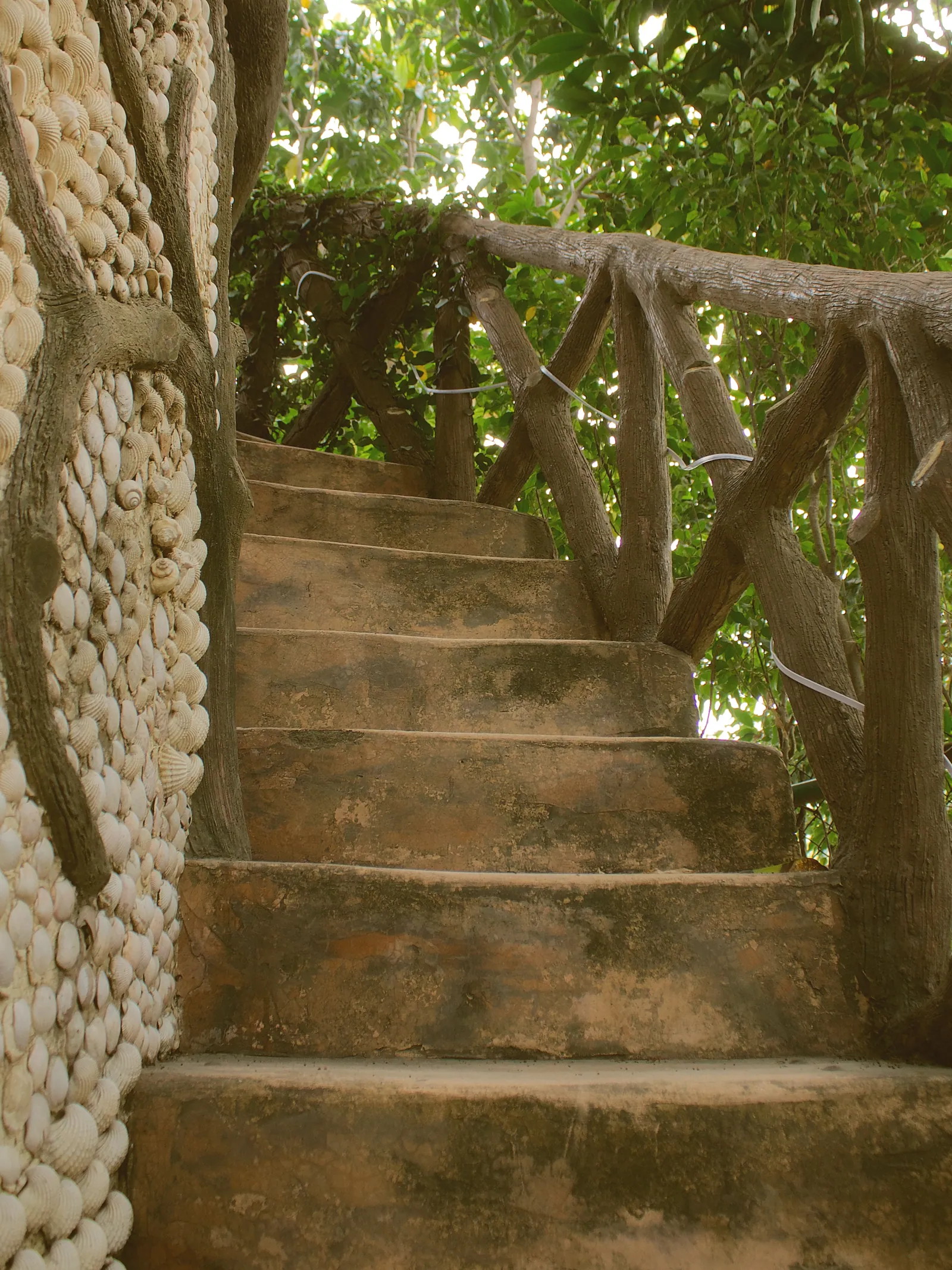 Rustic stone steps with a branch railing and a pebble-covered wall in the garden at Raj Organic Farm