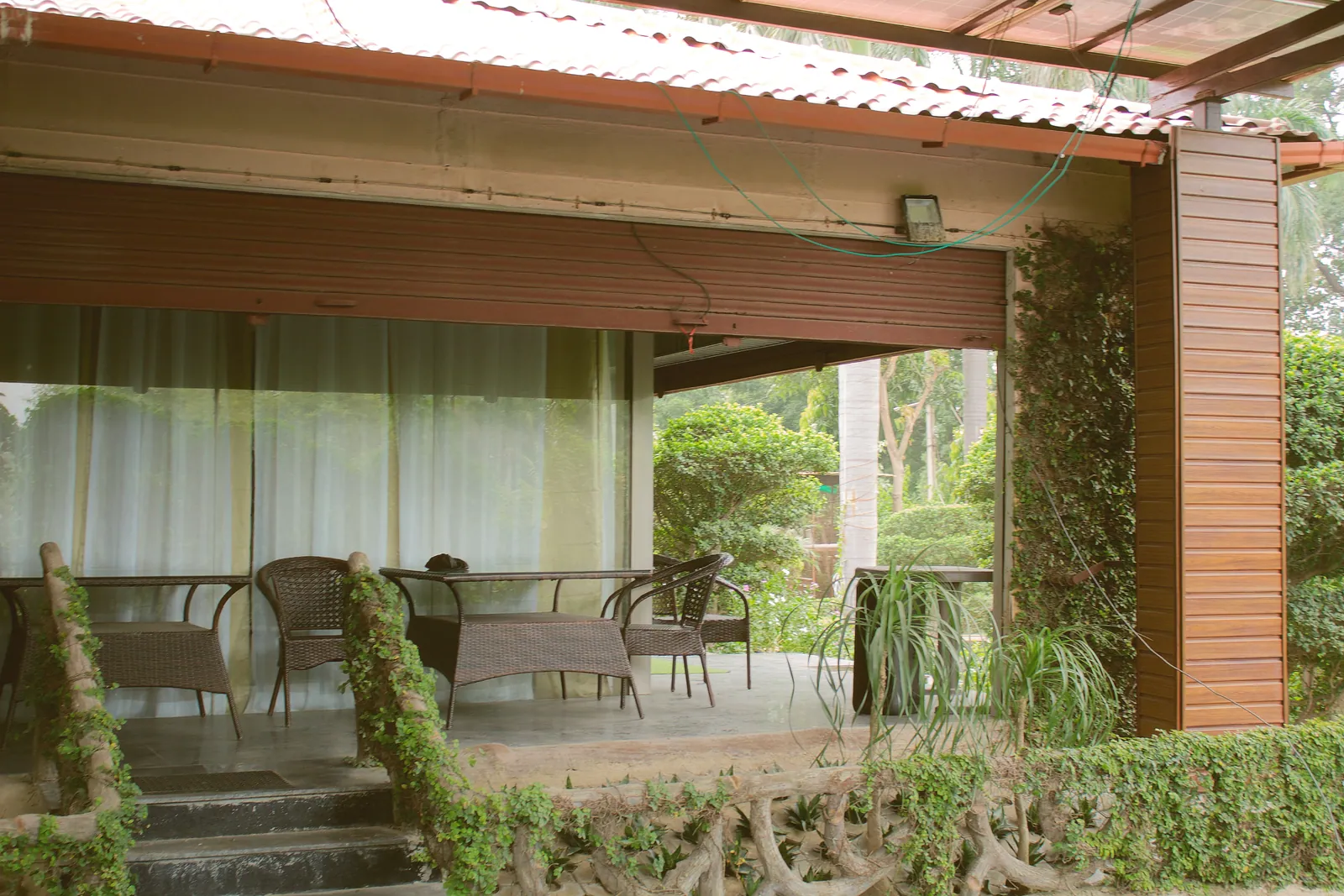 The covered veranda with wicker chairs and tables, long curtains and ivy-covered posts by day at Raj Organic Farm